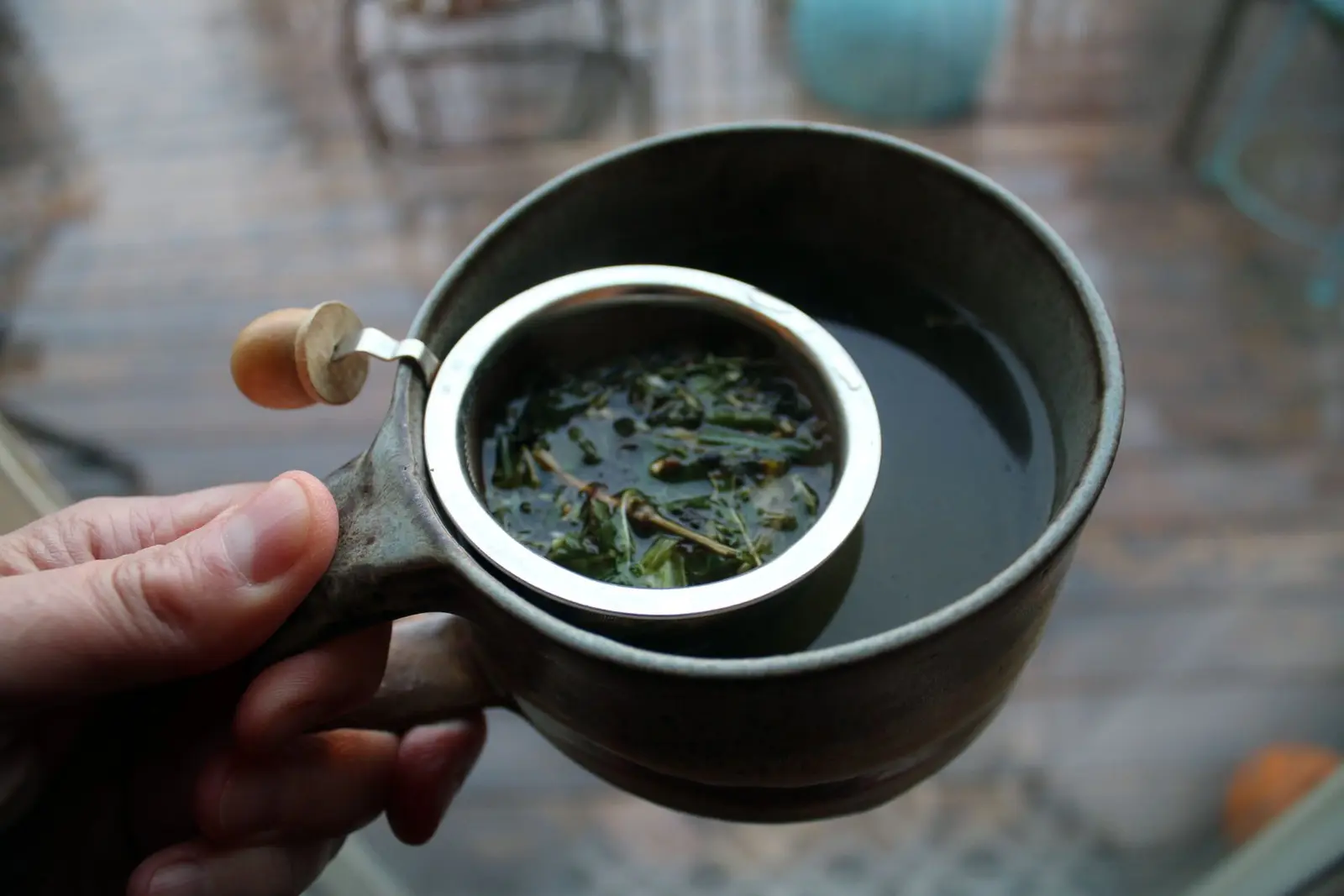 Hand holding a ceramic cup with a mesh tea infuser and green tea inside