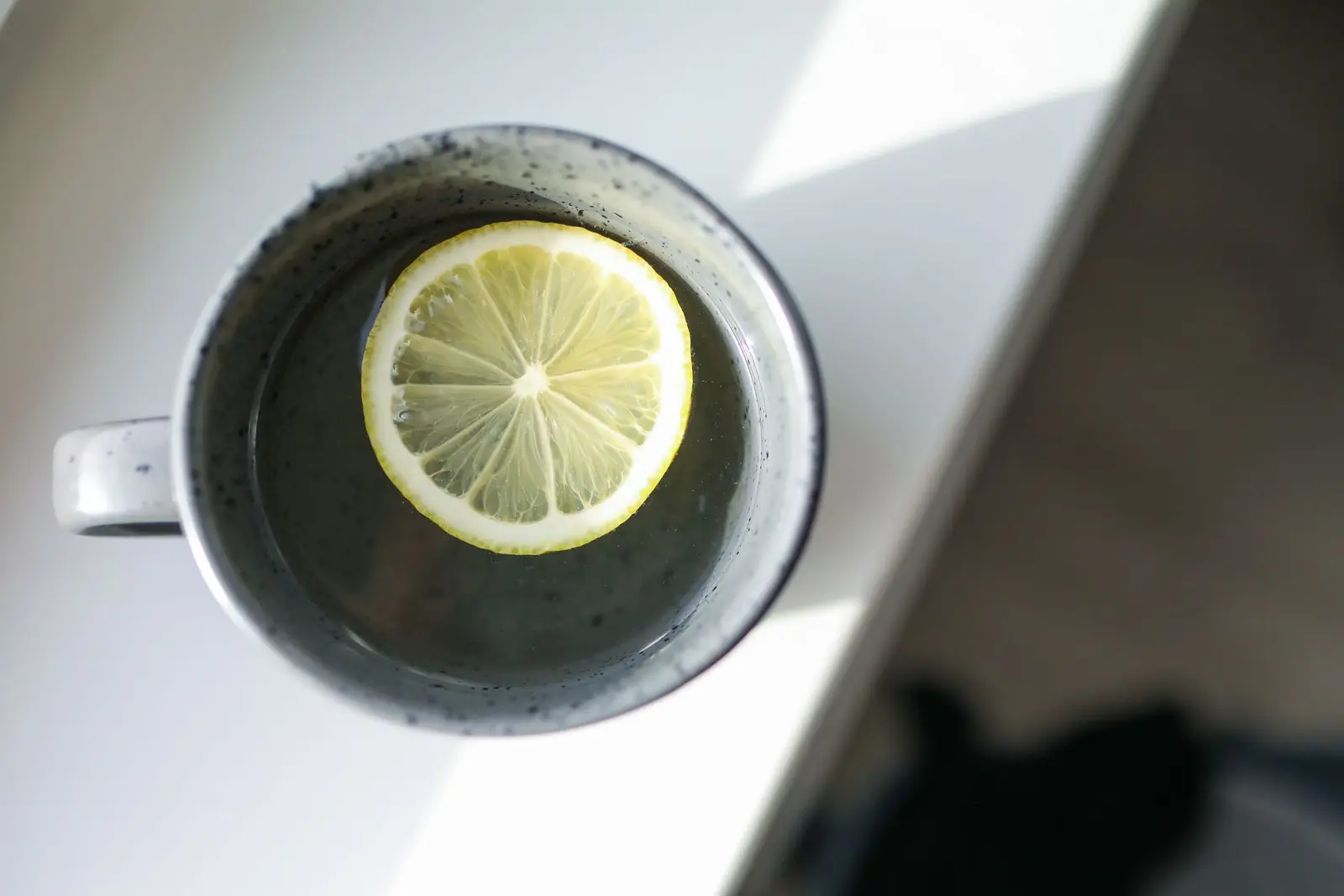 Top view of a dark ceramic mug of hot tea with a lemon slice