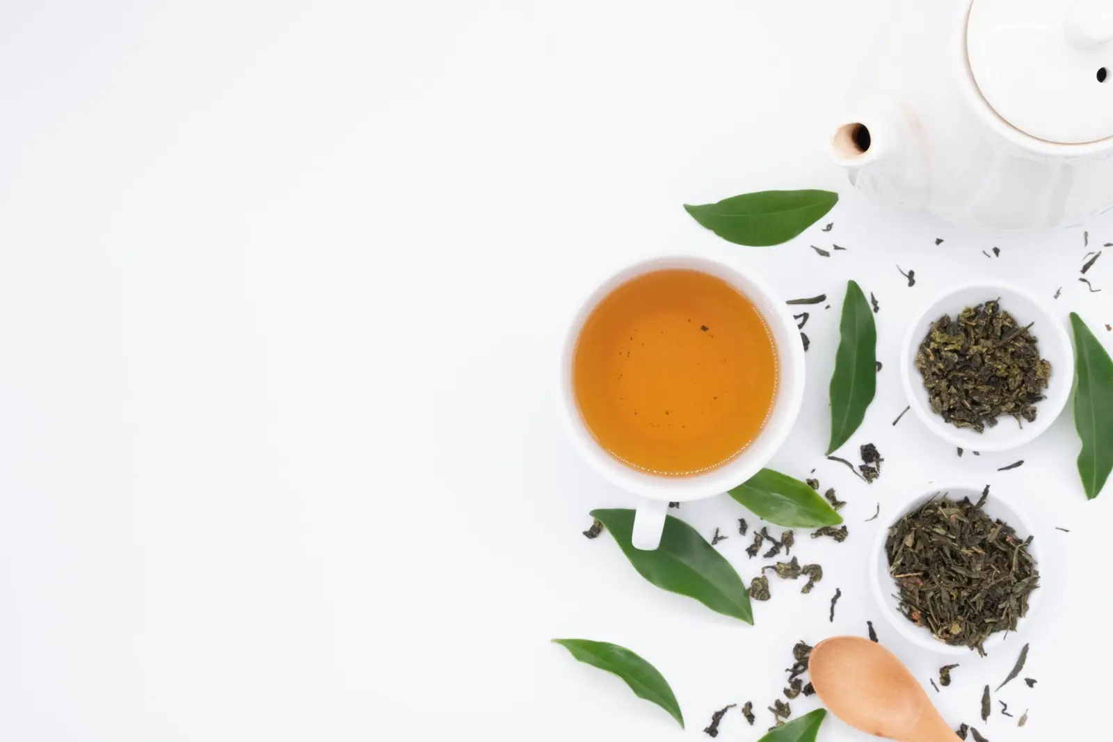 Cup of black tea beside small bowls of loose tea leaves and a wooden spoon on a white background