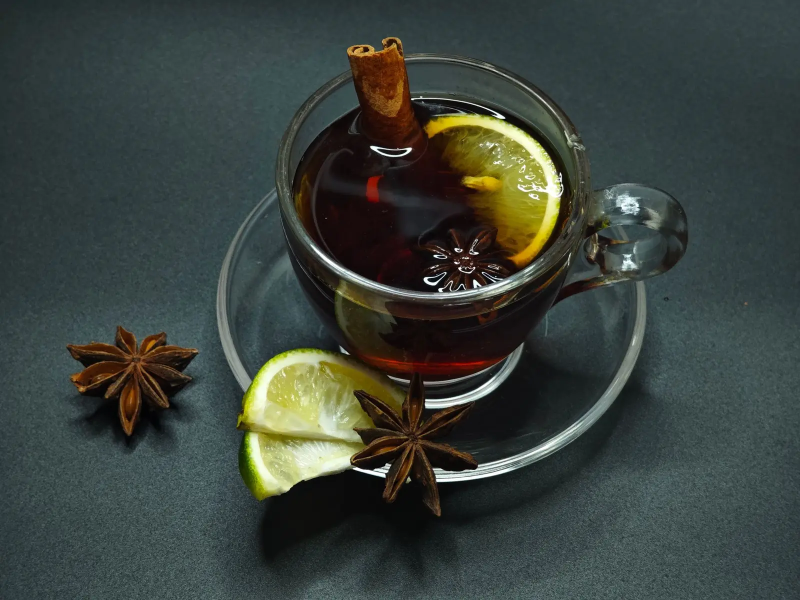 Spiced black tea in a glass cup with a cinnamon stick, star anise and lemon slices on a dark surface