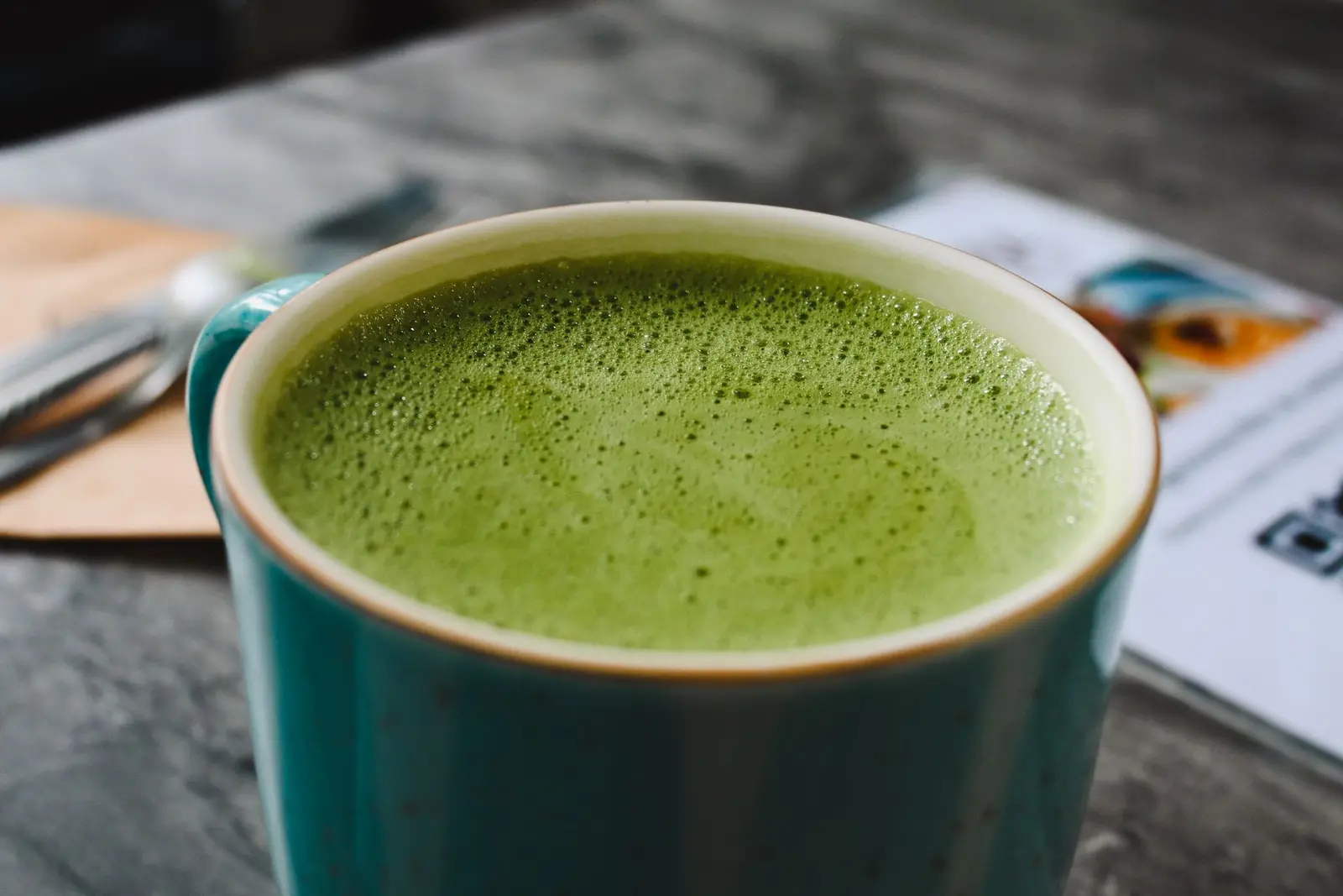 Close-up of a frothy matcha latte in a teal ceramic cup