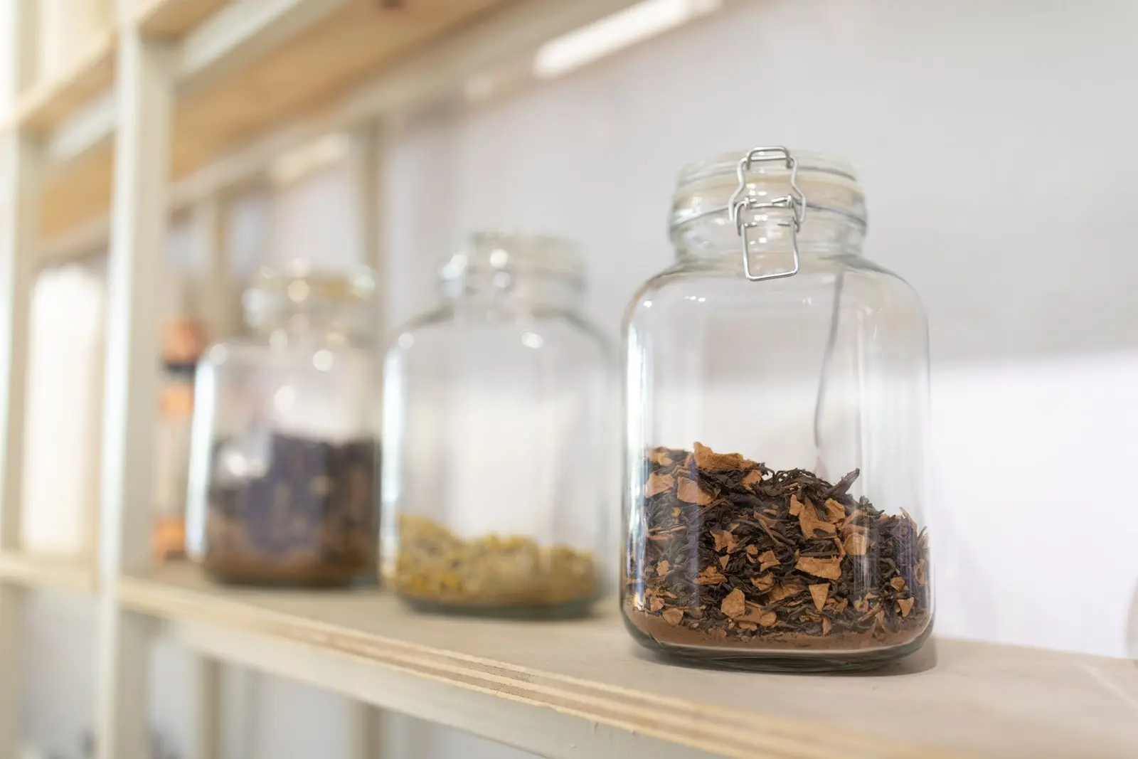 Glass storage jars filled with loose tea and dried herbs on a wooden shelf