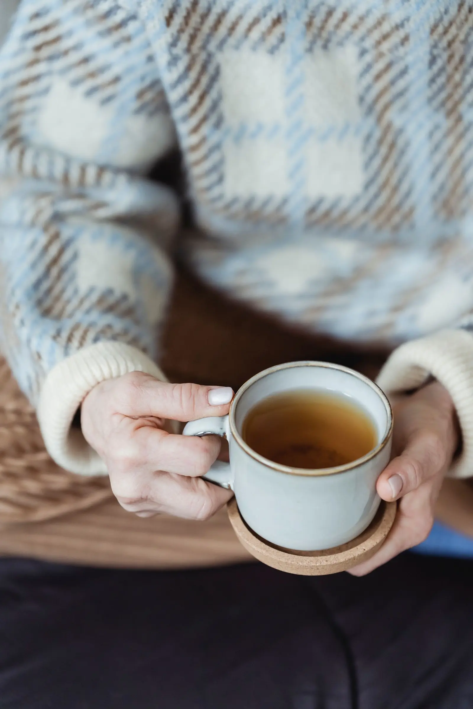 Person in a knitted sweater holding a cup of tea in both hands