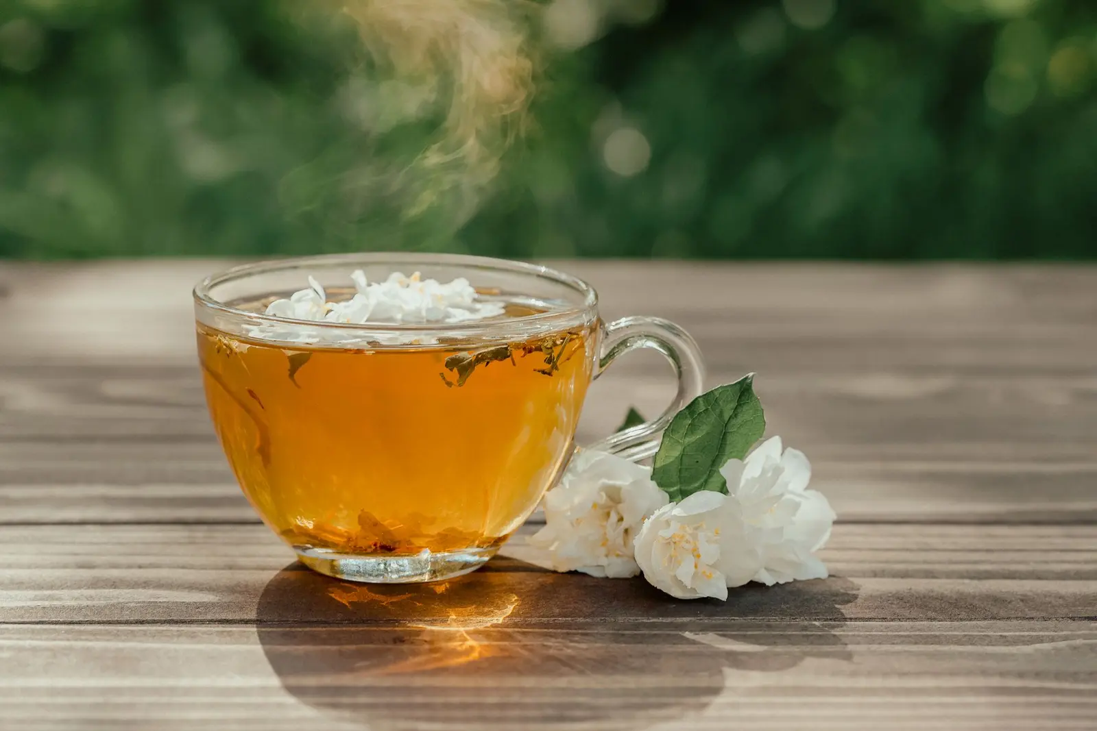 Glass cup of golden jasmine tea with white jasmine blossoms on a wooden table