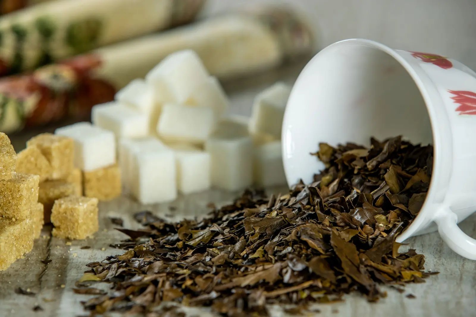 Loose black tea leaves spilling from a white cup beside sugar cubes