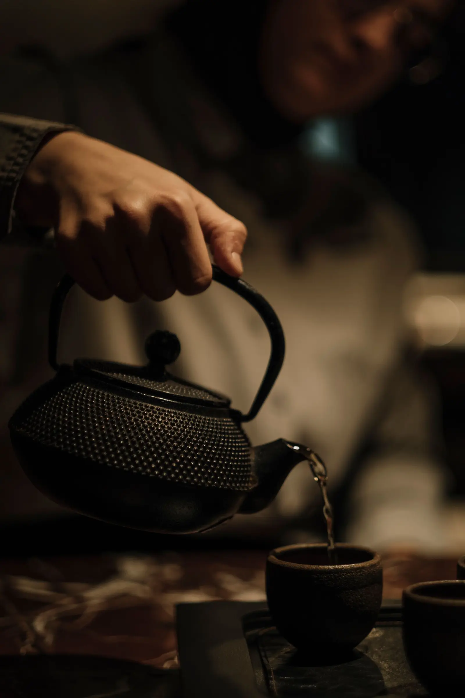 Hand pouring hot water from a cast-iron kettle into a small cup