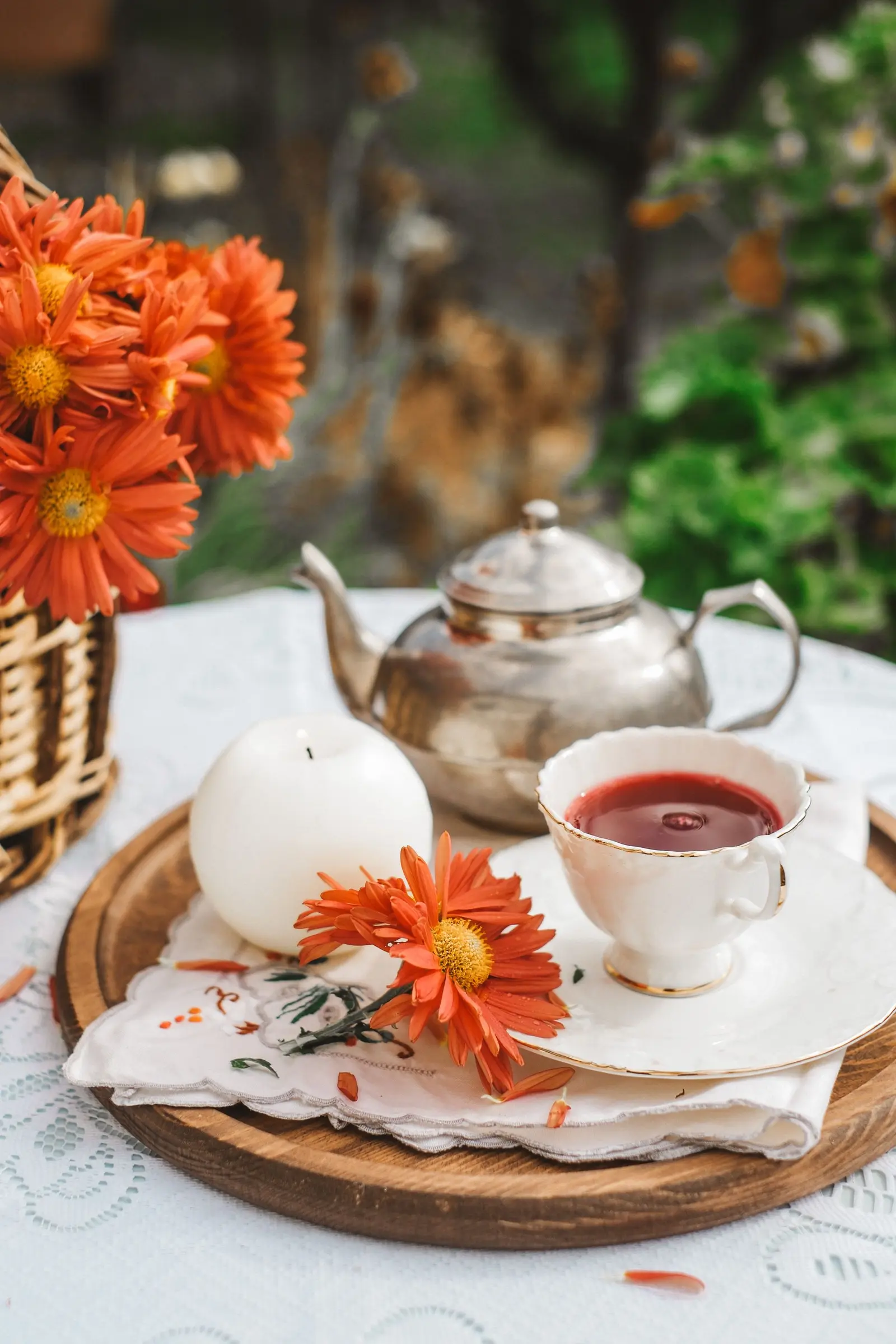 Cup of red tea with a silver teapot, a candle and orange flowers on a wooden tray